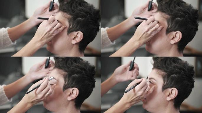 化妆师的手的特写视图用刷子为中年模特画眉毛，短发假睫毛。慢动作镜头