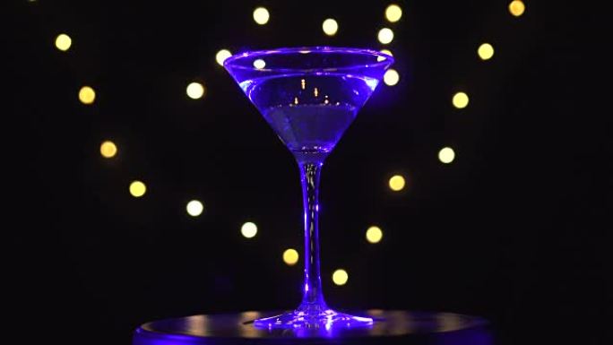 玻璃中明亮的蓝色鸡尾酒，在黑暗的背景下旋转，光线模糊。