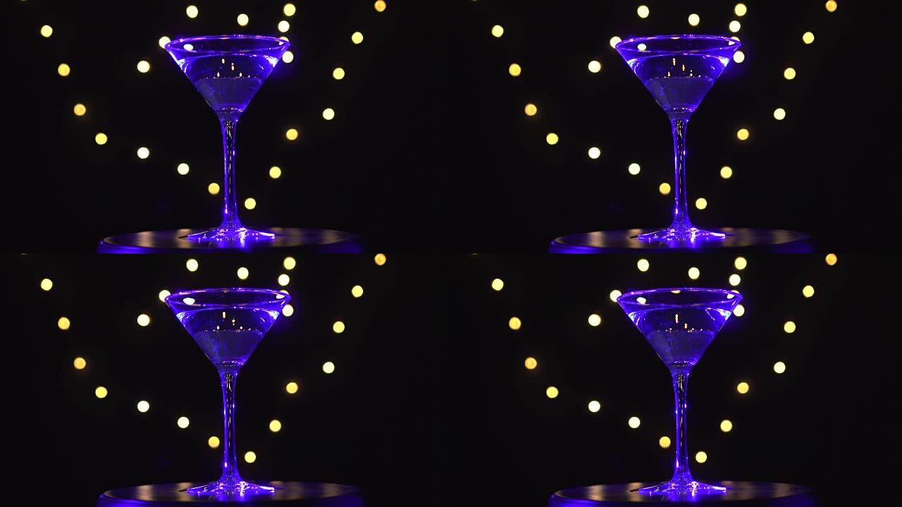 玻璃中明亮的蓝色鸡尾酒，在黑暗的背景下旋转，光线模糊。