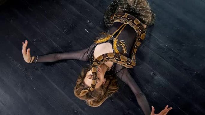 穿着鲜艳服装的迷人女人与蛇躺在地板上跳舞