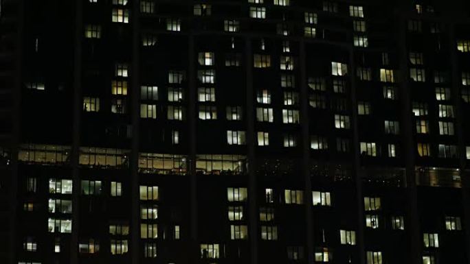 黑暗中的办公楼。窗户亮着，人们的轮廓可见。倾斜镜头
