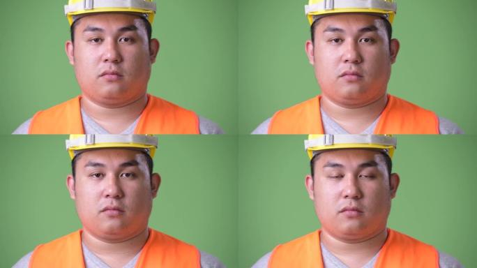 绿色背景下年轻英俊超重的亚洲男子建筑工人