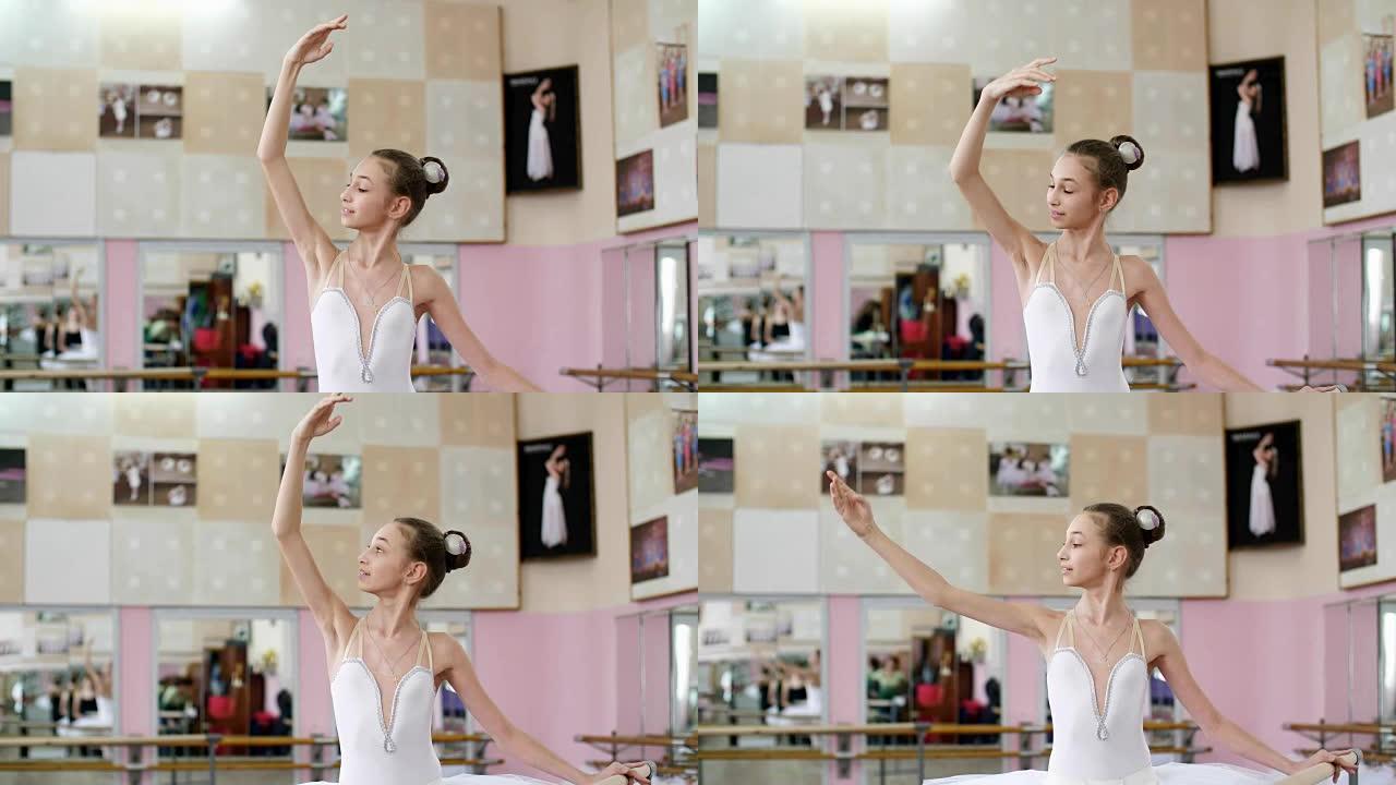 在芭蕾舞大厅里，穿着白色芭蕾舞短裙的女孩，pack参加芭蕾舞，排练胸罩，优雅地上下举手，年轻的芭蕾舞