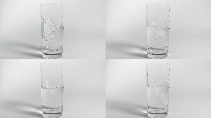 两块冰落入透明的清水玻璃中。慢动作