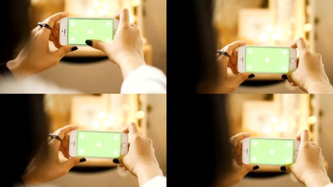 女人的手在房间里触摸带有色度键绿色屏幕的智能手机时的特写-绿色屏幕手持智能手机