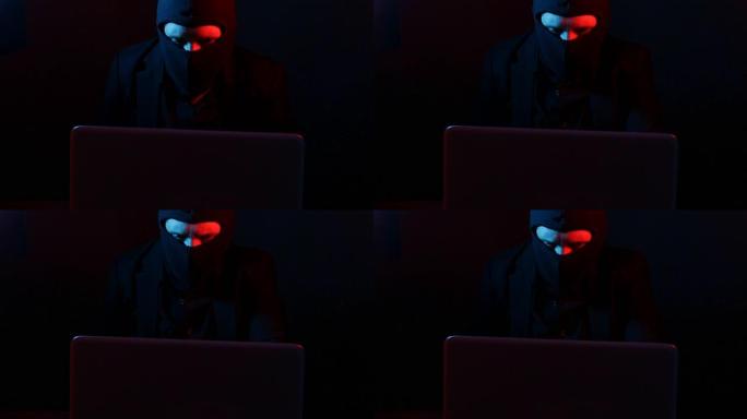 穿着西装的愤怒的计算机黑客从红色和蓝色灯光照亮的笔记本电脑中窃取数据