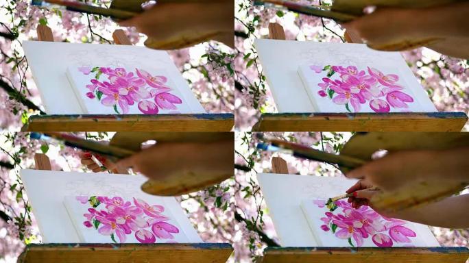 特写镜头，画家在盛开的春天苹果园里画了一幅花，她用画笔画画，用颜料拿着调色板。风席卷画架上的开花树枝