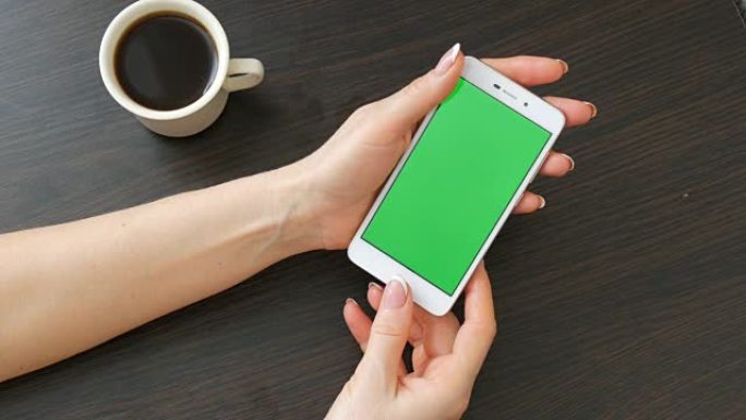 女性手与美丽的法式美甲采取一个白色智能手机与绿屏附近的白杯咖啡。使用智能手机，将带有绿色屏幕的智能手
