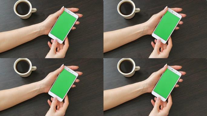女性手与美丽的法式美甲采取一个白色智能手机与绿屏附近的白杯咖啡。使用智能手机，将带有绿色屏幕的智能手
