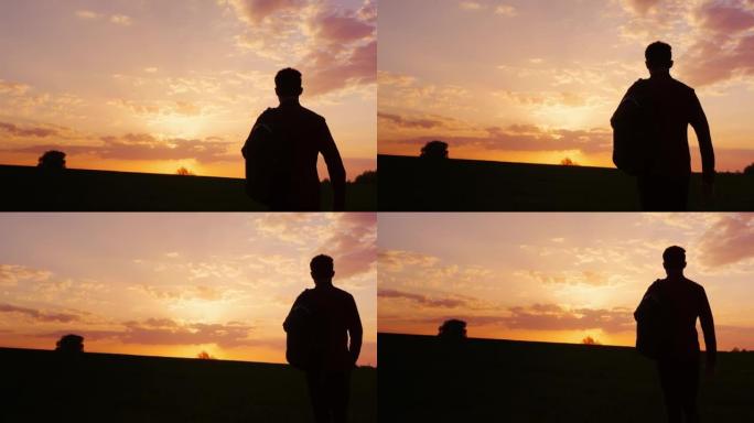 一个背着背包的少年在田野或乡村走向日落。剪影视频，后视图。概念-新的研究，前进到未知，离开家