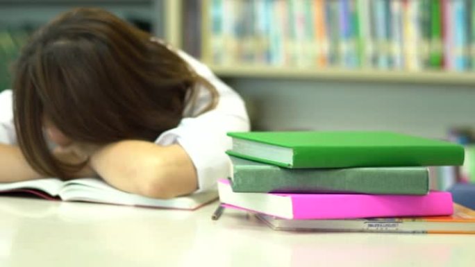 亚洲女学生在睡觉和醒来时在学校图书馆看书