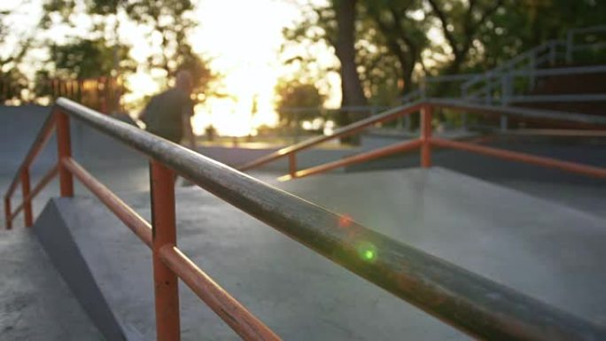 日落时在混凝土滑板公园里玩花样的滑板手的剪影，慢动作