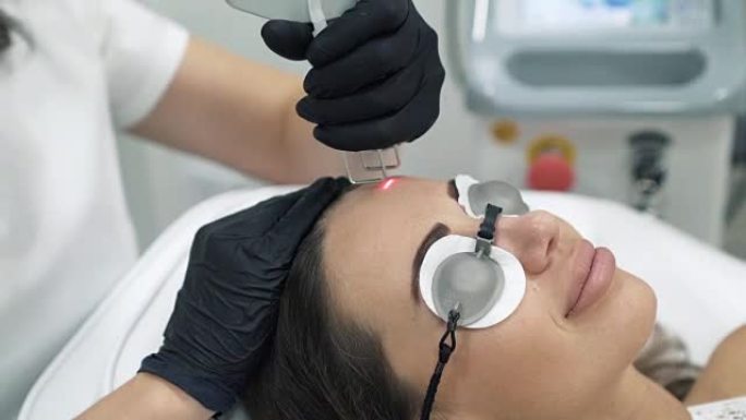 医生美容师穿着晨衣和手套在女性病人的脸上执行激光程序特写。整形和扩张手术，门诊皮肤置换。无菌室里的医