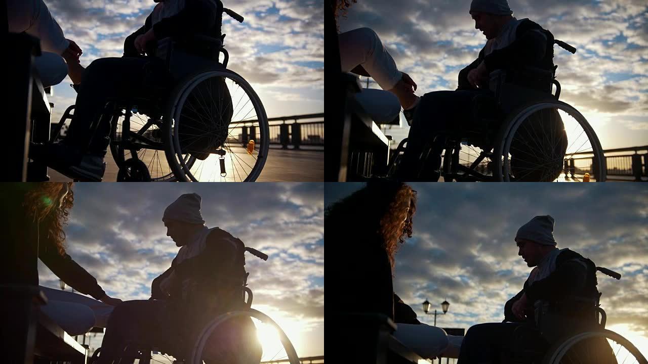 年轻女子与残疾男子坐在轮椅上的剪影在户外日落时交谈