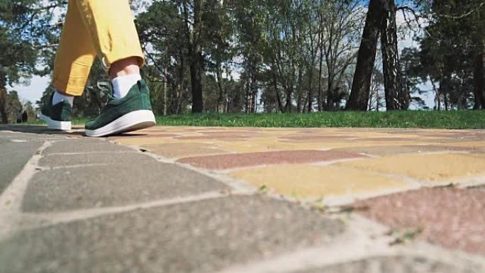 穿着绿色运动鞋和黄色裤子的女性腿沿着公园的小路行走，慢动作。