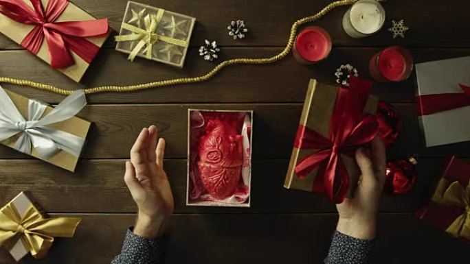 惊讶的男人在装饰的木桌上打开带有解剖塑料人体心脏的圣诞礼物盒，自上而下拍摄