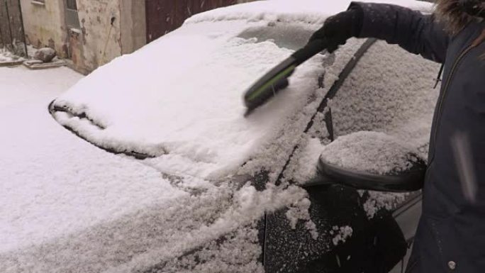 下雪天汽车附近有刷子的女人