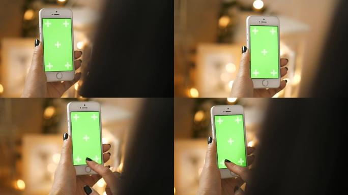 女人的手在房间里触摸带有色度键绿色屏幕的智能手机时的特写-绿色屏幕手持智能手机