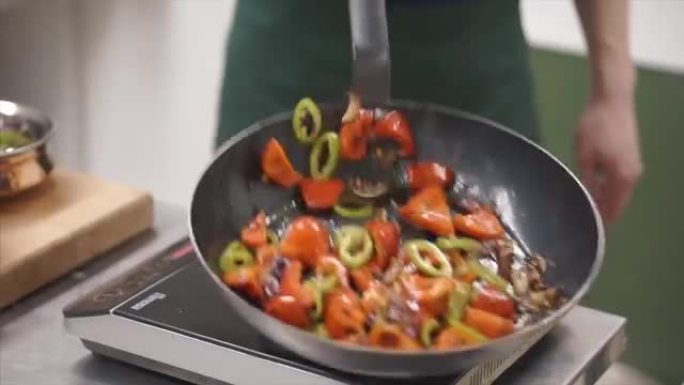 厨师特写镜头在炒锅里烹饪食物 -- 蔬菜和肉做面条饭。夹。用明火在平底锅里油炸新鲜蔬菜。扔甜菜叶，胡