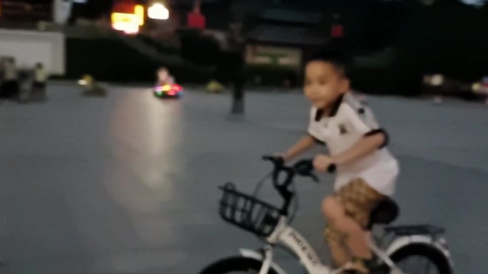 夜晚骑自行车的小男孩小孩在闹市区骑踩单车