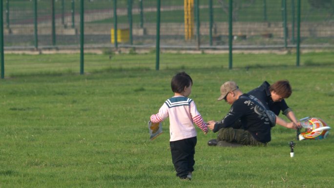 一个小孩子在草地上奔跑大人在后面追温馨