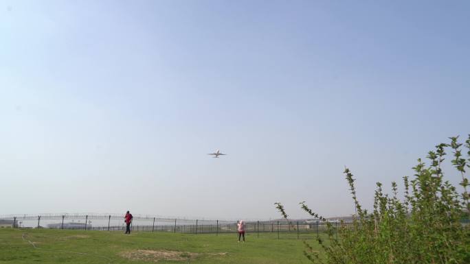 透过机场围栏飞机飞过游客拿手机拍照