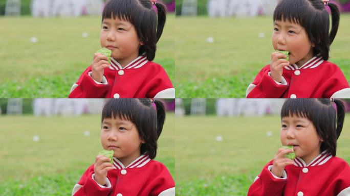 坐在草坪上小口品尝东西的可爱小女孩