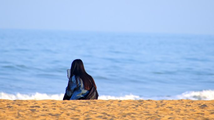 坐在海边玩手机的少女