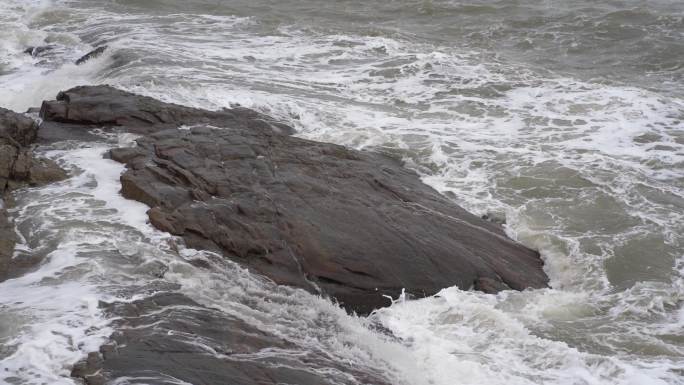 海浪拍打岩石浑浊海水冲刷礁石浪花阴天大海