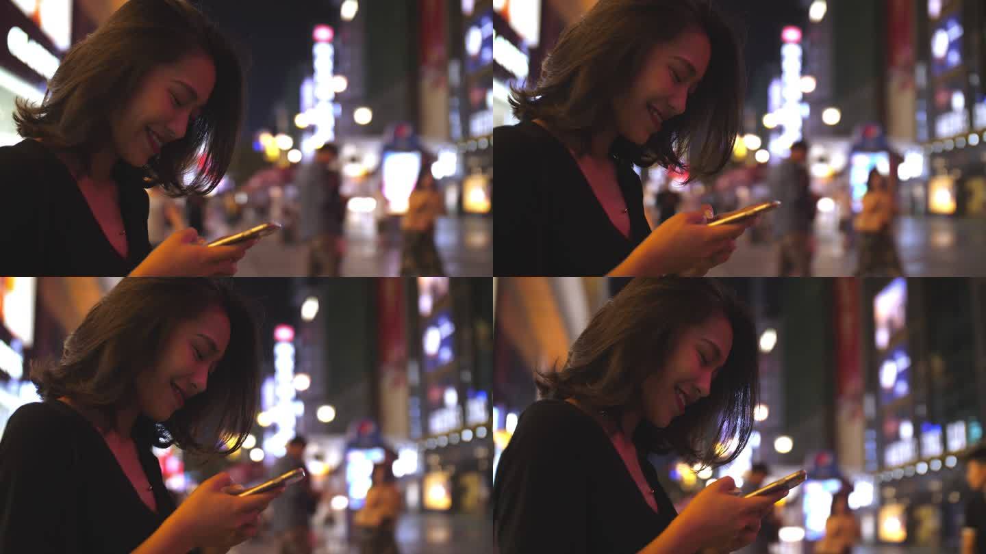 美女夜晚城市街头看手机微笑