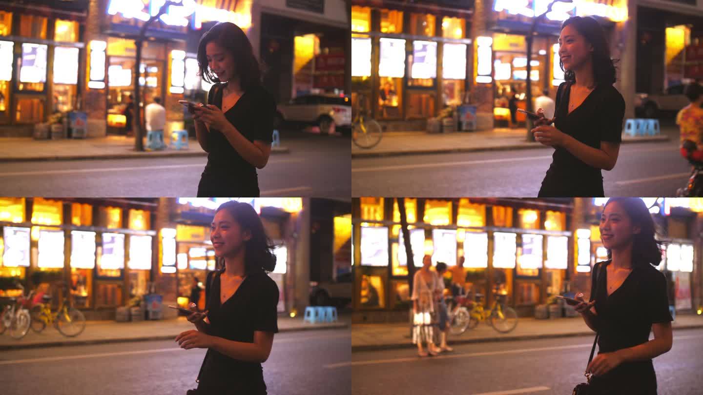 夏日晚上美女走在城市街头看手机