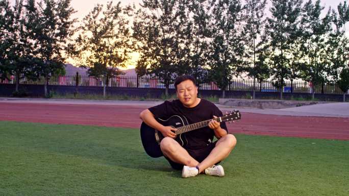 坐在操场弹奏吉他唱歌的中年歌手