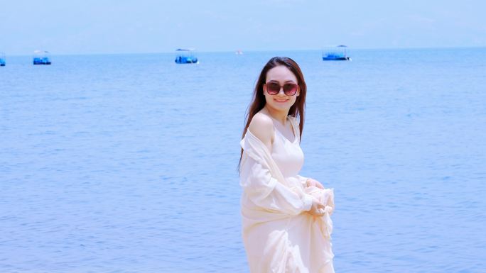 身穿白色裙子戴着墨镜在海边沙滩散步的美女