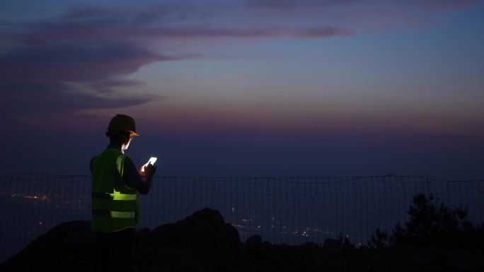 夕阳下工程师在山顶使用手机