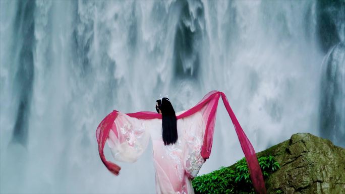 女生站在瀑布前张开双臂拥抱瀑布裙子飞扬