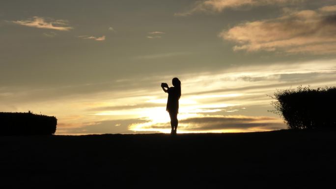 女生在山坡上飞无人机夕阳落日下的剪影航拍