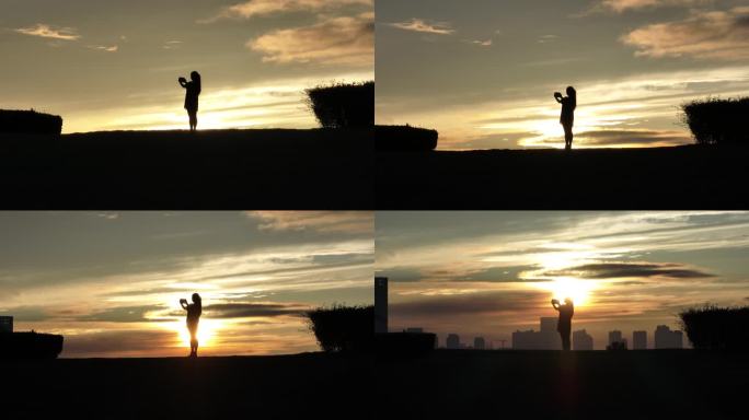 女生在山坡上飞无人机夕阳落日下的剪影航拍