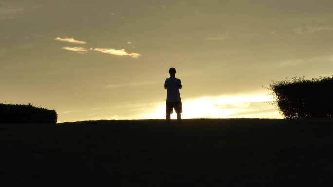 男生在山坡上飞无人机夕阳落日下的剪影航拍
