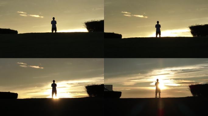 男生在山坡上飞无人机夕阳落日下的剪影航拍