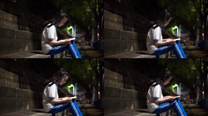 晚上中学生坐在台阶路灯下看书认真读书复习