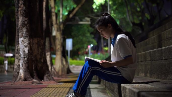 晚上中学生坐在台阶路灯下看书认真读书复习