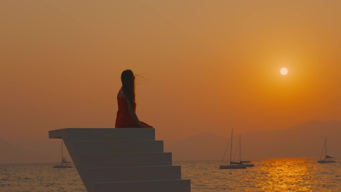 高台上夕阳下海边海风中看日落的女孩