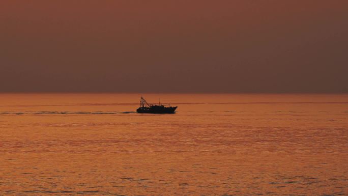 北海海上落日余晖下缓慢行驶的一艘渔船