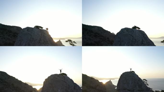 克里米亚日出时，一位年轻女子在海边爬山的空中剪影。夫人举手站在山顶上，风景秀丽.