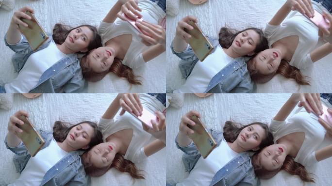 两个漂亮的亚洲朋友在床上玩手机的俯视视频，消费技术的概念正在迅速发展。