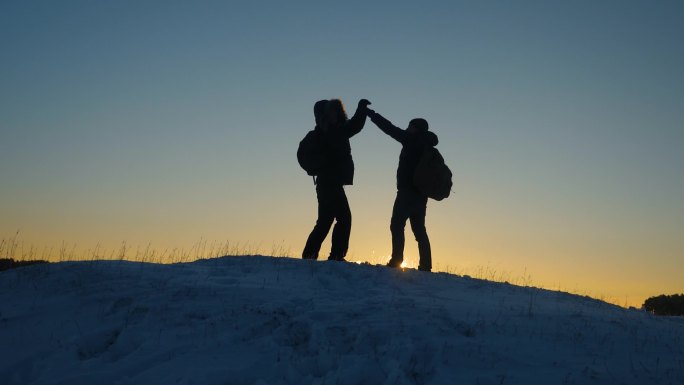 登山者在雪山山顶相遇, 享受他们的成功, 举起双手快乐地跳。男人游客背着背包在冬天的日落到达山顶。体