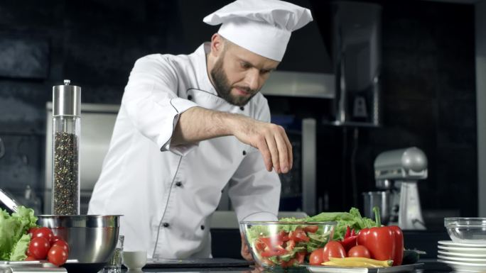 厨师用慢动作调味蔬菜。厨师在厨房烹饪新鲜食物.