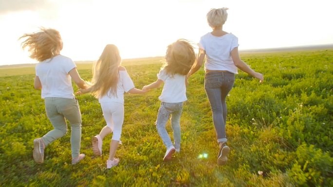 友情概念。年轻快乐的妇女与他们的女儿跑过田野在日落