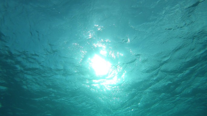 慢动作，水下，视点: 仰望平静的太平洋闪耀的表面。明亮的太阳光照亮了法属波利尼西亚附近广阔的热带海洋
