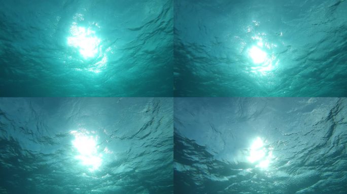 慢动作，水下，视点: 仰望平静的太平洋闪耀的表面。明亮的太阳光照亮了法属波利尼西亚附近广阔的热带海洋